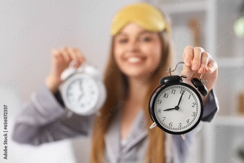 Happy young woman in pajamas with alarm clocks on bed at home