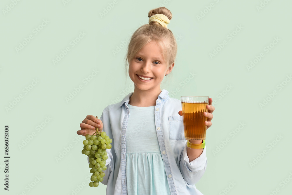 Little girl with glass of juice and grapes on green background