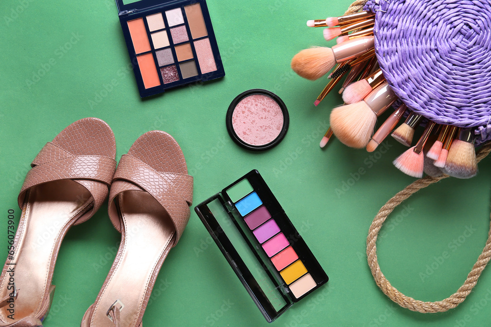 Composition with female shoes, cosmetics and makeup brushes on green background