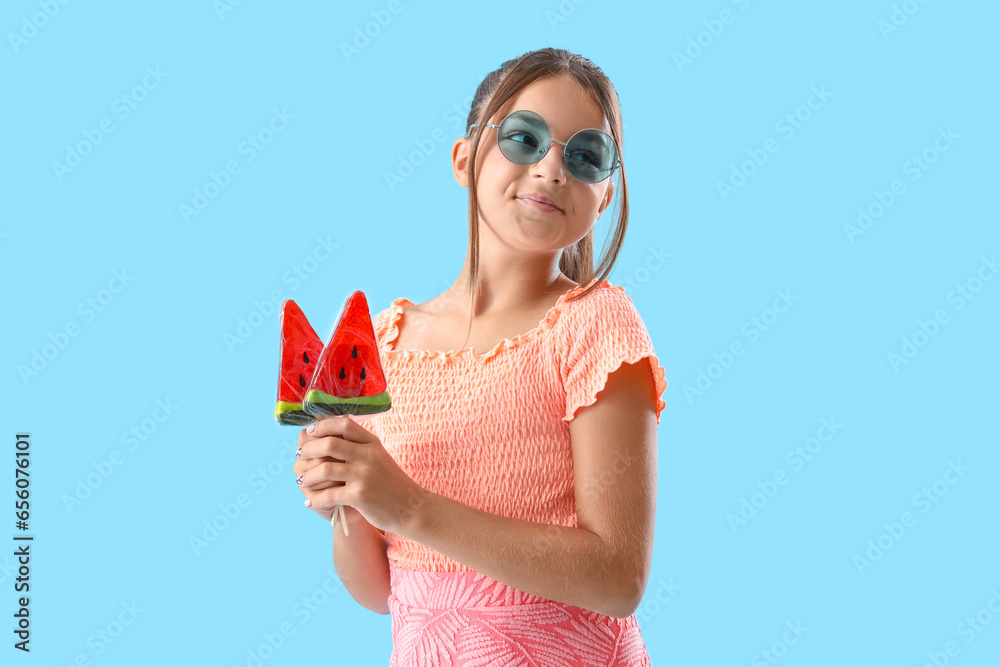 Happy little girl with lollipops in shape of watermelon slices on blue background