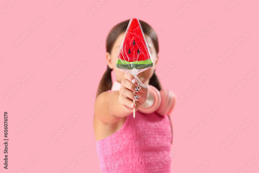 Little girl with lollipop in shape of watermelon slice on pink background