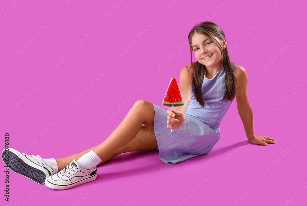 Happy little girl with lollipop in shape of watermelon slice sitting on purple background