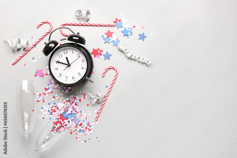 Alarm clock with Christmas candy canes, glasses and confetti on white background