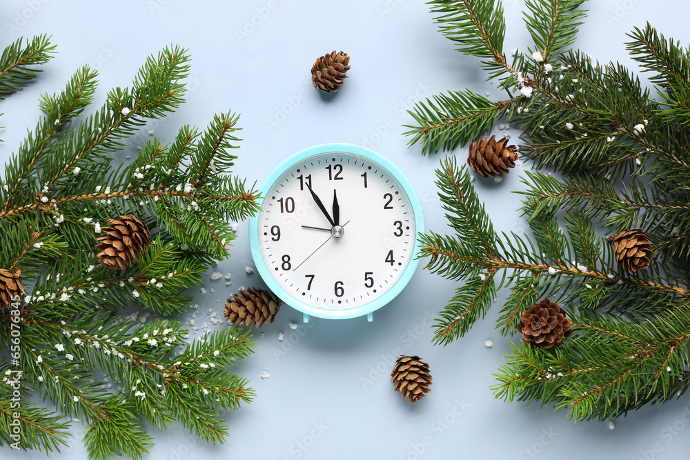 Alarm clock and Christmas tree branches with cones on blue background