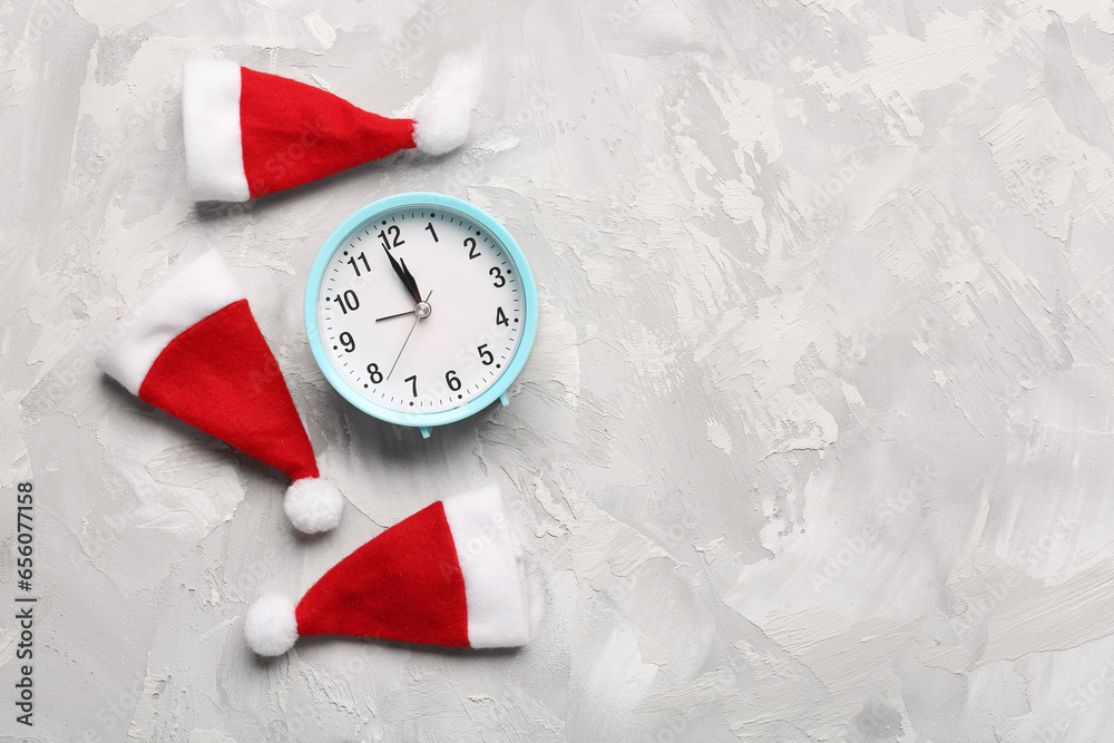 Alarm clock and Santa hats on grey background