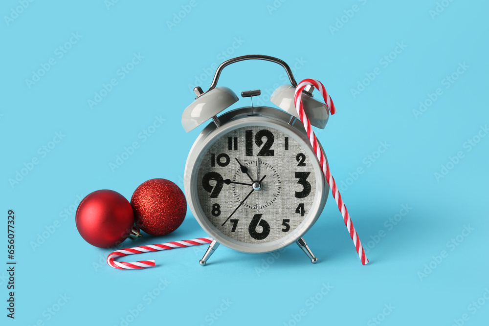 Alarm clock with Christmas balls and candy canes on blue background