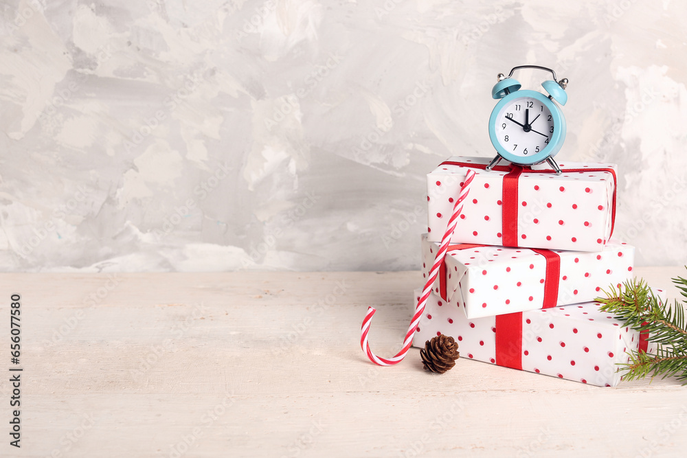 Alarm clock with Christmas gift boxes and candy cane on white wooden table