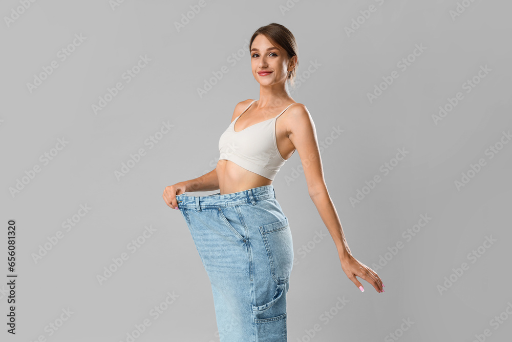 Beautiful young woman in loose jeans on grey background. Weight loss concept