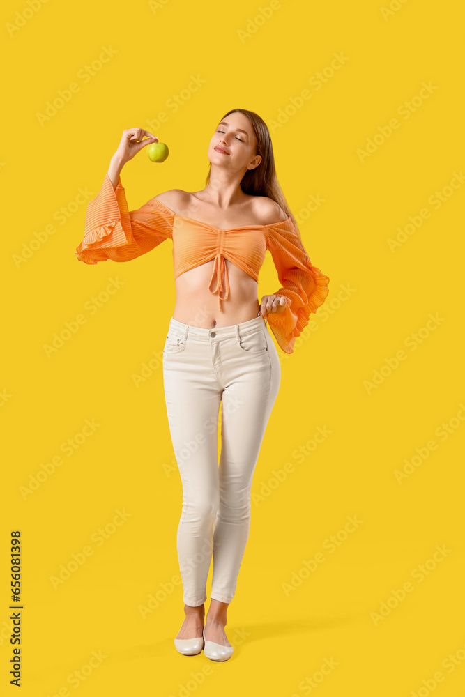 Beautiful young woman with fresh apple on yellow background. Weight loss concept