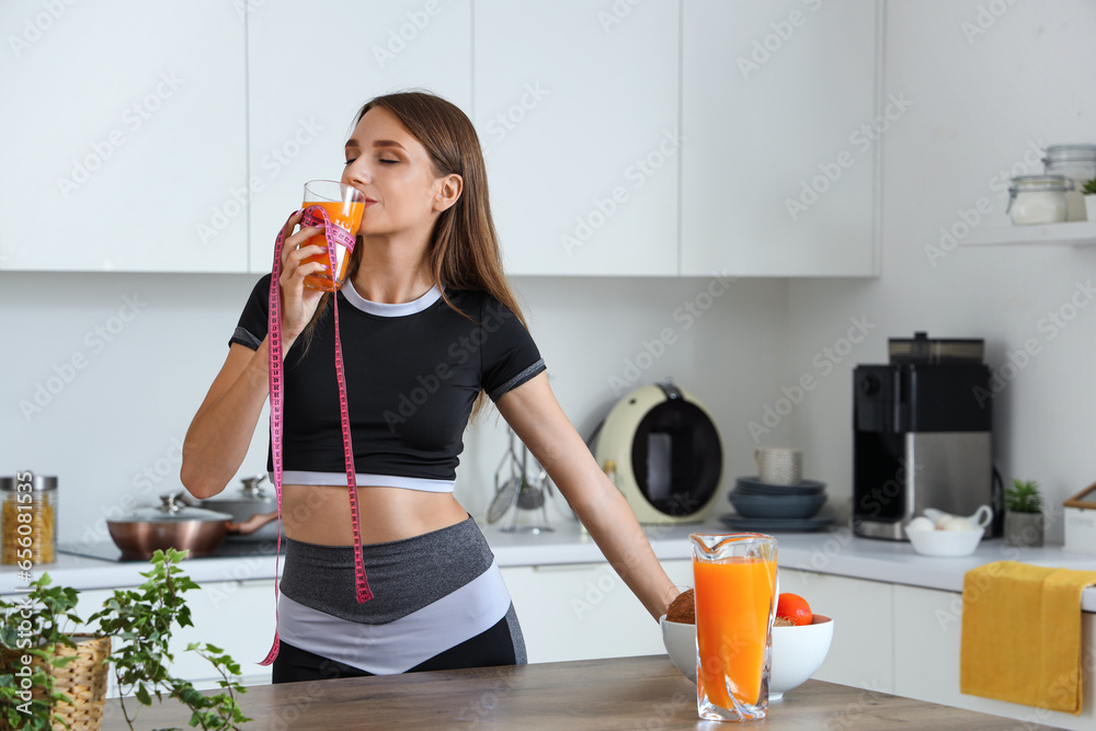 Beautiful young woman with measuring tape drinking healthy juice in kitchen. Weight loss concept