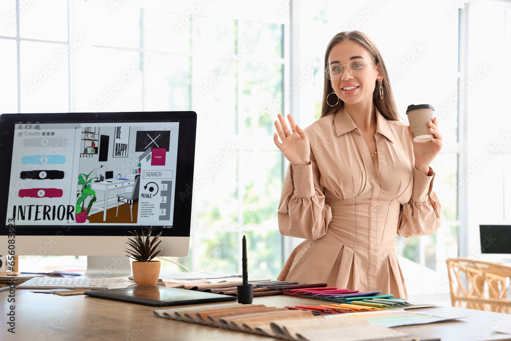 Female interior designer with cup of coffee working at table in office