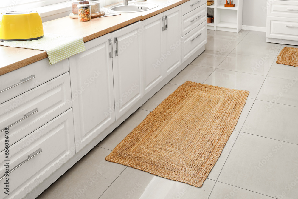 Interior of light kitchen with white counters and wicker carpet