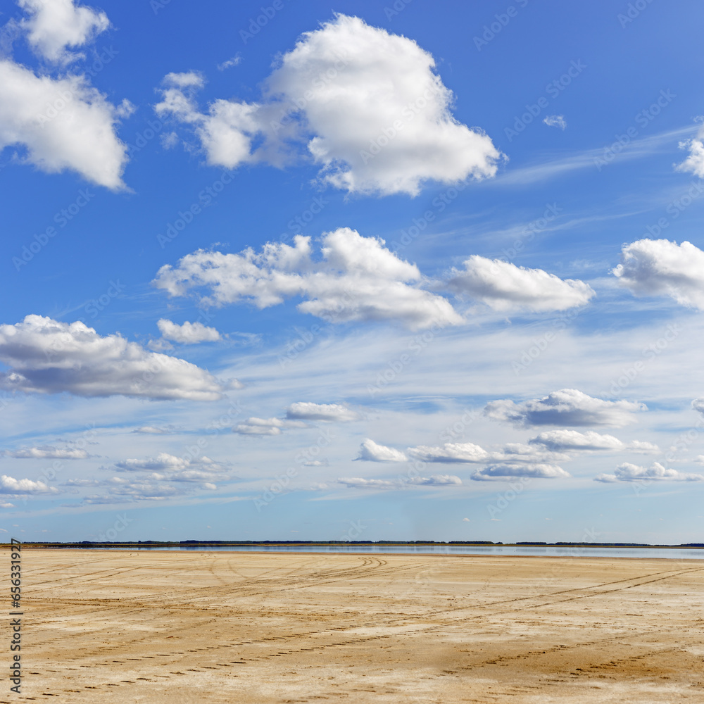 Beautiful shore of lake, white clouds on sky, water surface and sandy beach. Tranquil nature scene, summer sunlight day. Vibrant colored landscape in minimal style, panoramic cloudscape