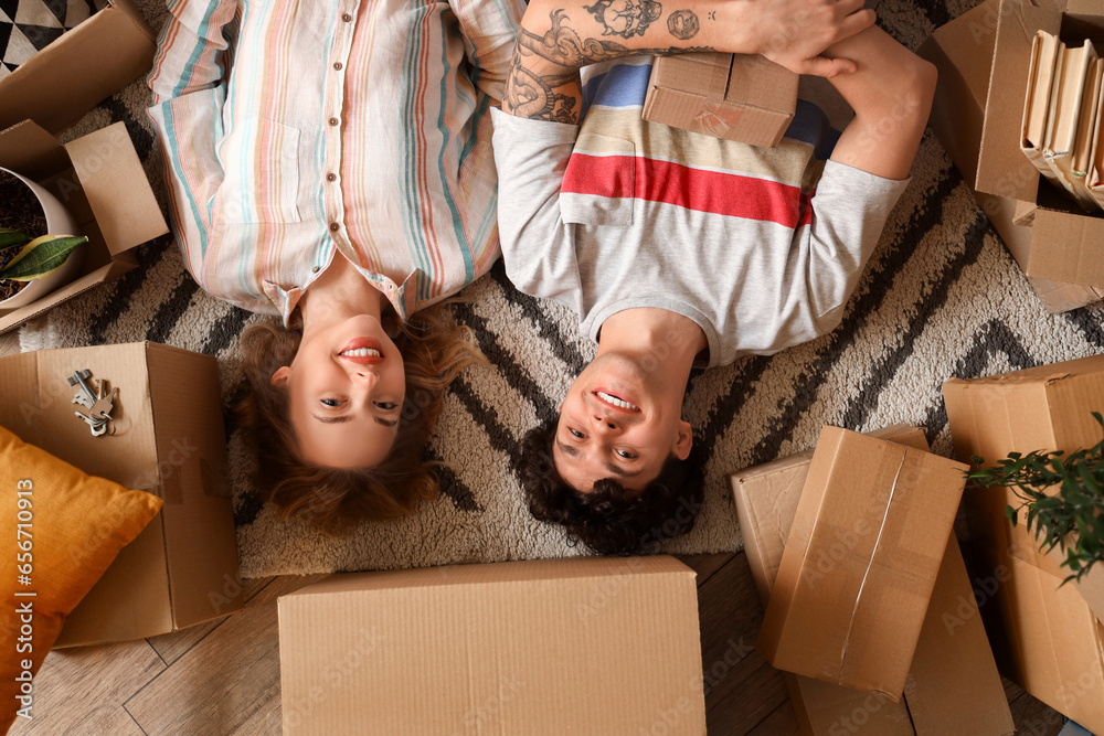 Young couple with moving boxes lying on carpet, top view