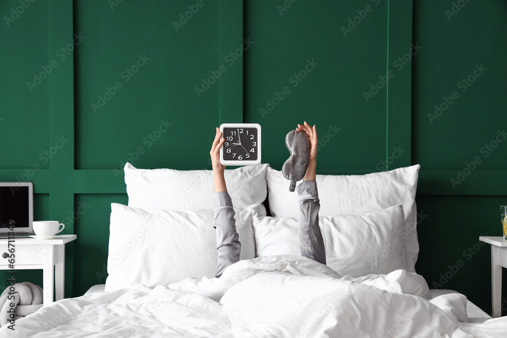 Morning of young woman with clock and sleeping mask in bed