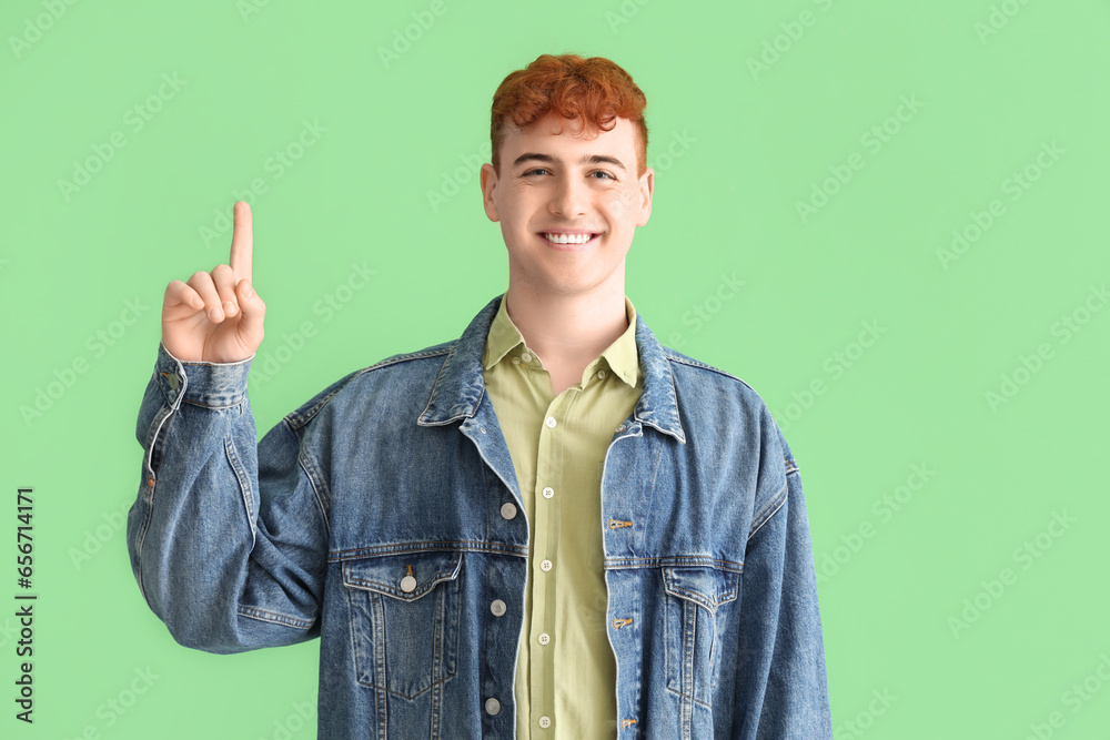 Young redhead man pointing at something on green background