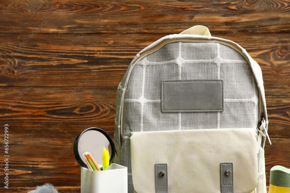 Grey school backpack with cup of pens and magnifying glass on wooden background