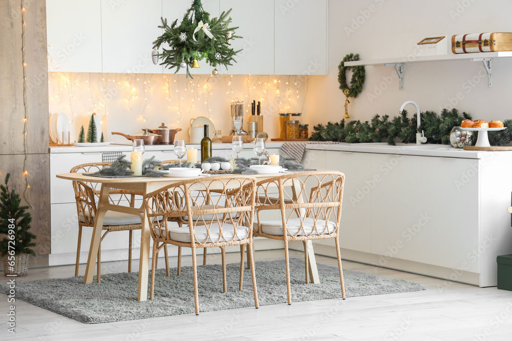 Interior of modern kitchen with festive table setting, glowing lights and Christmas decorations