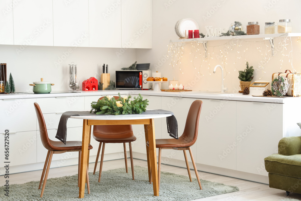 Interior of modern kitchen with festive table setting, glowing lights and Christmas decorations