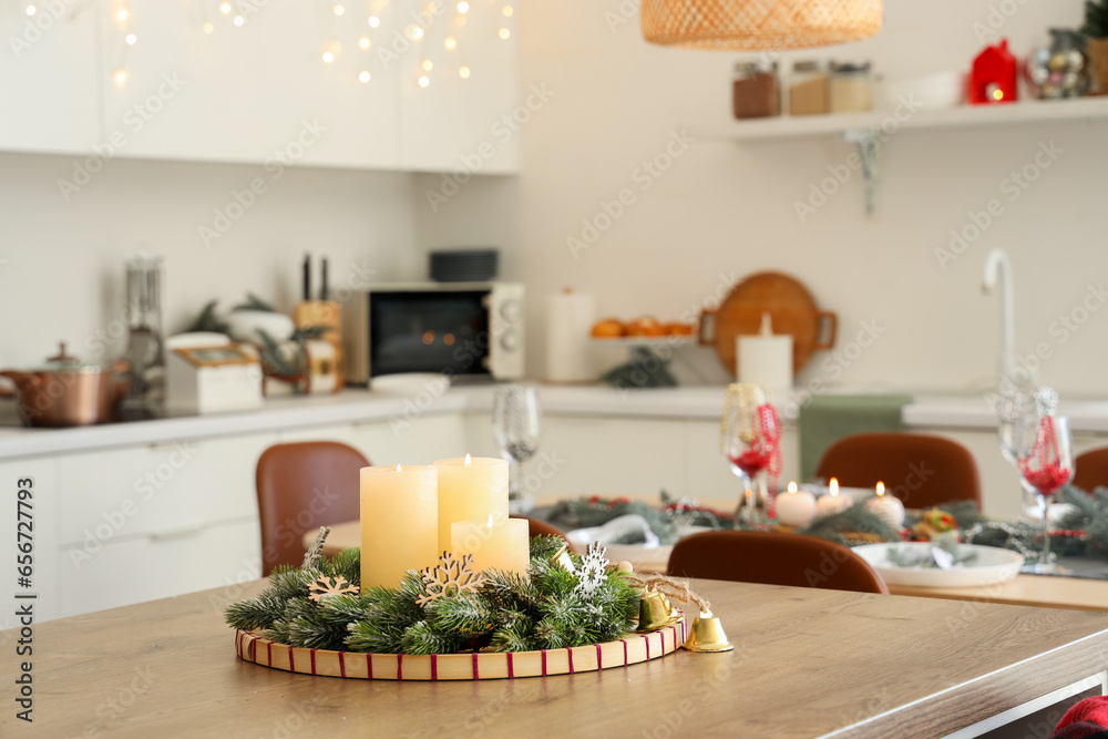 Burning candles and Christmas wreath on wooden table in kitchen, closeup