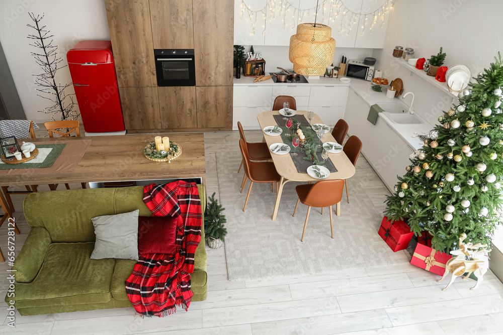 Interior of festive kitchen with Christmas tree, green sofa and served dining table