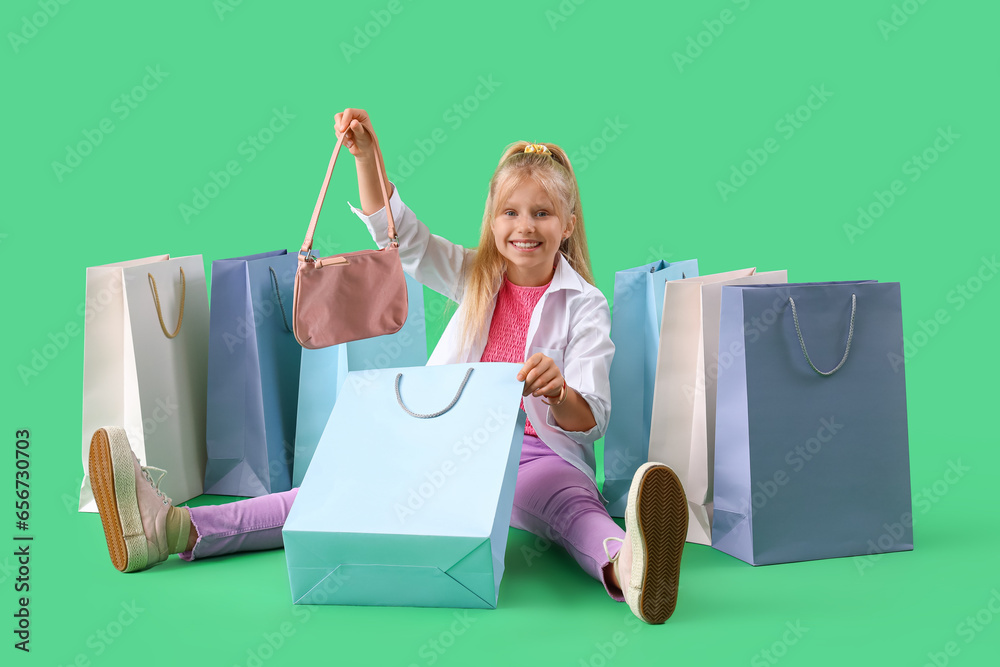 Little girl with shopping bags sitting on green background