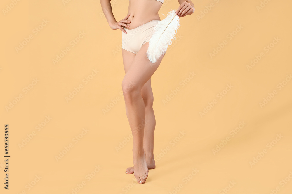 Young woman with shaved legs and feather on beige background