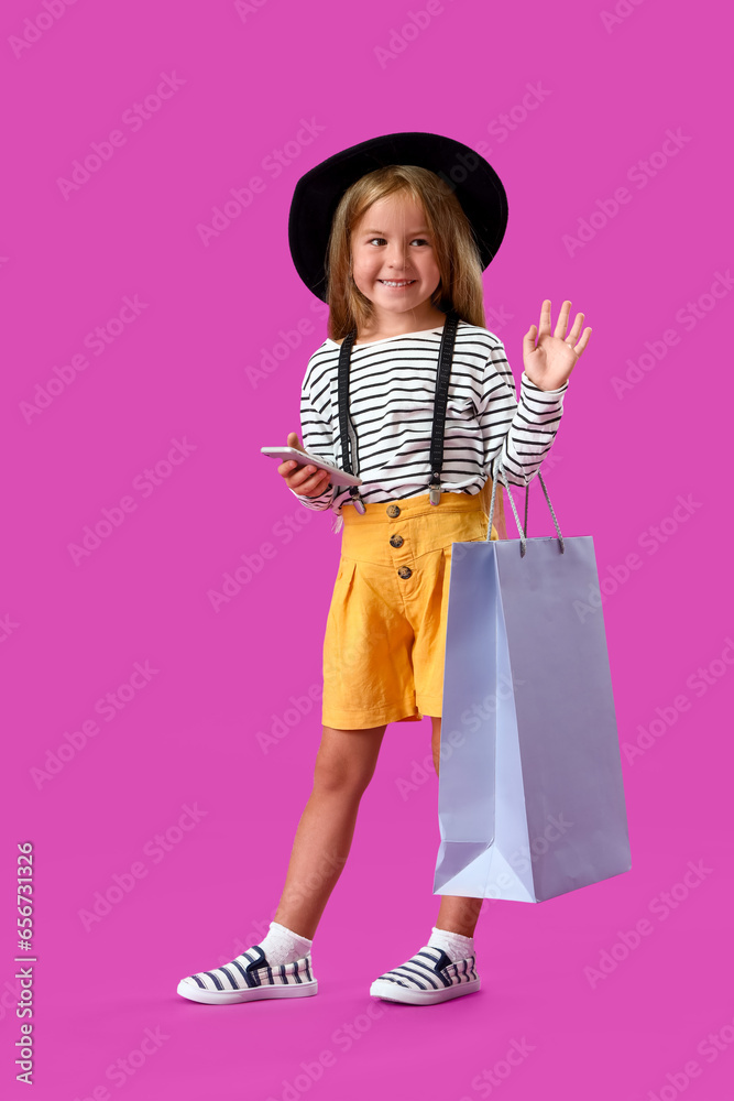 Cute little girl with mobile phone and shopping bag on purple background