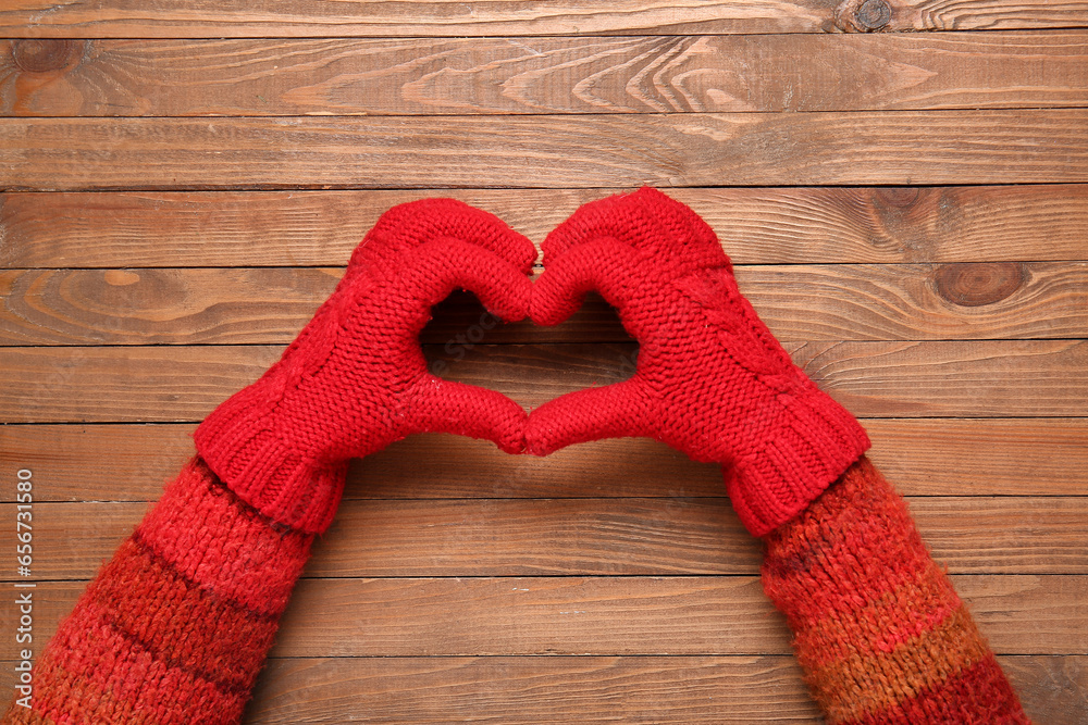 Woman in warm gloves making heart shape with her hands on wooden background, closeup