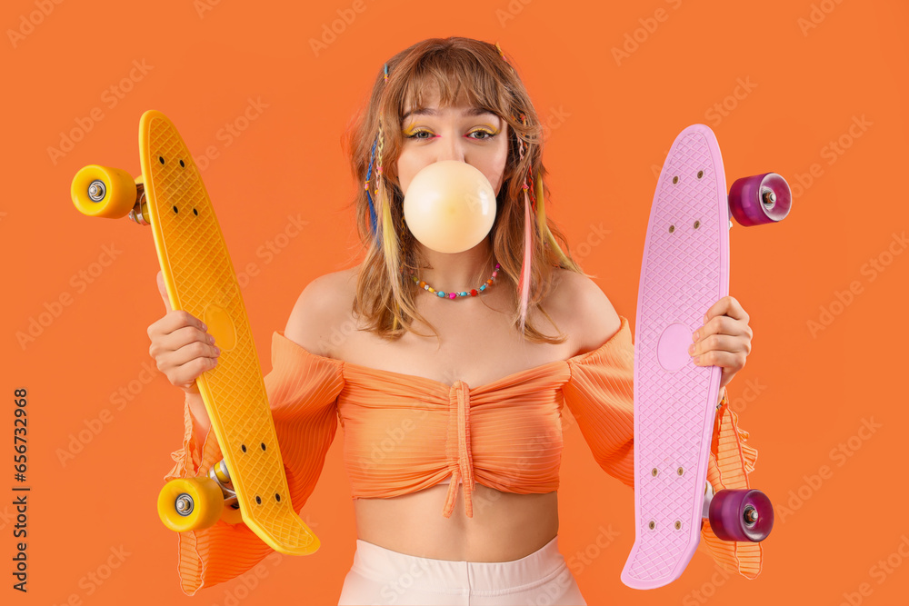 Young woman with chewing gum and skateboards on orange background