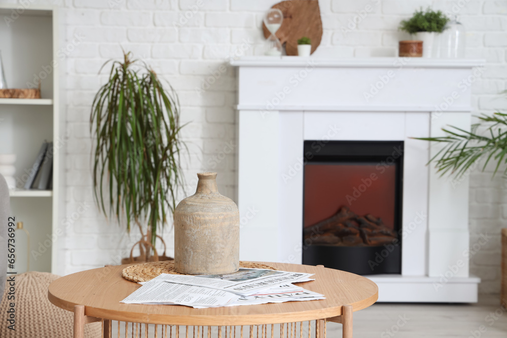 Table with stylish vase and newspapers near modern fireplace in living room