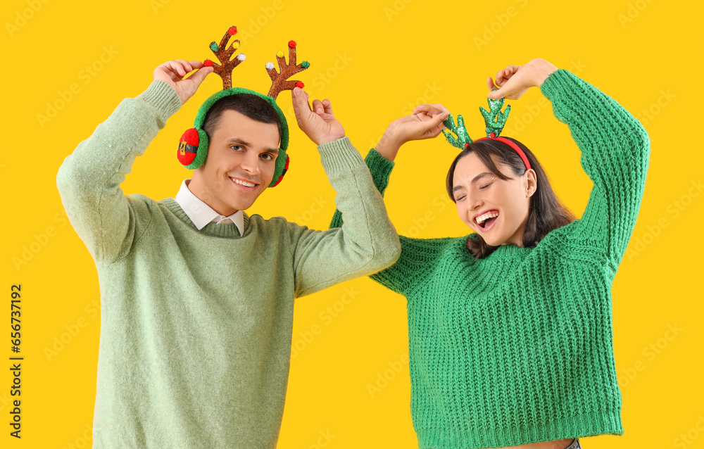 Happy beautiful young couple in Christmas reindeer horns on yellow background