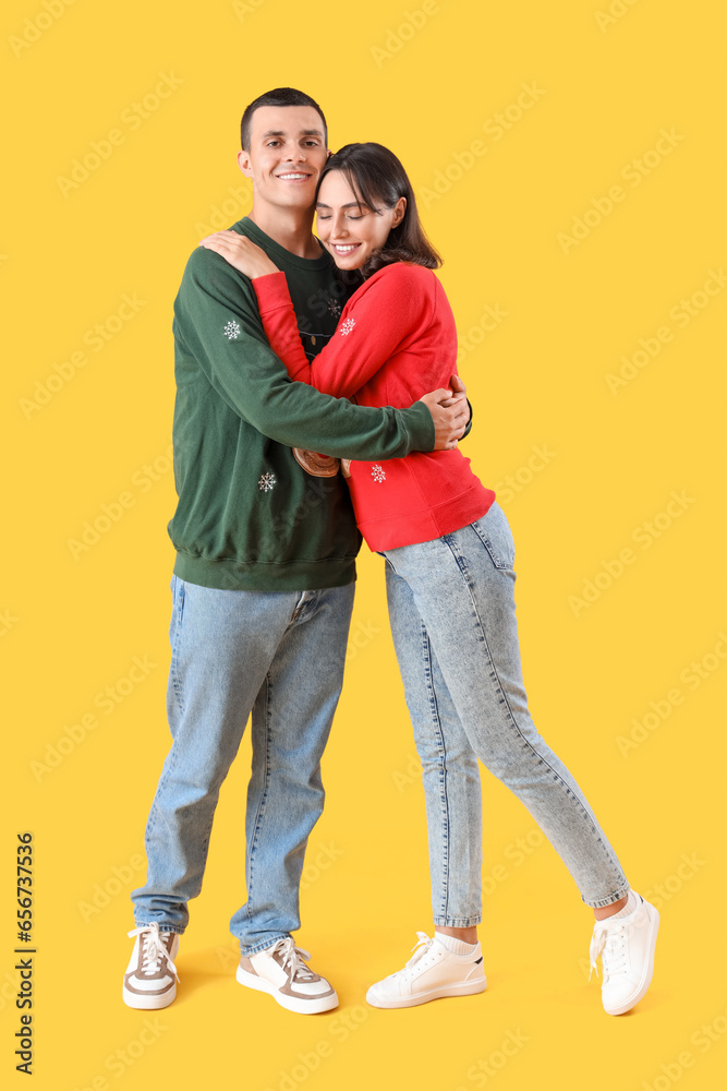 Beautiful young couple in Christmas clothes hugging on yellow background