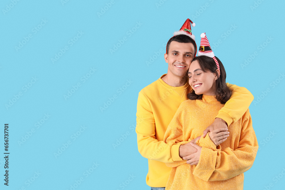 Happy young couple in Christmas hats hugging on blue background