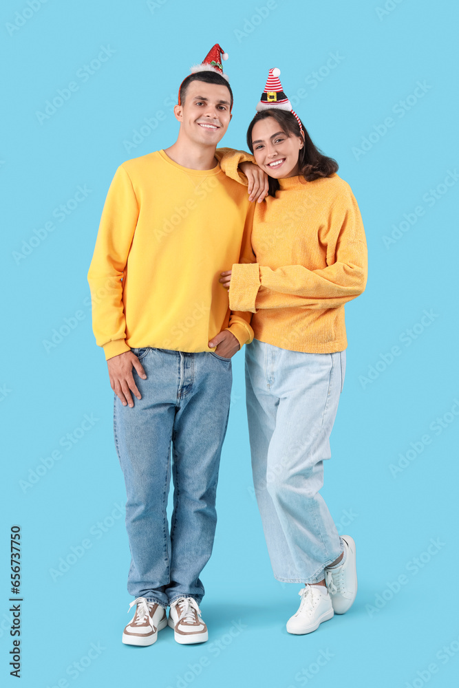 Happy young couple in Christmas hats on blue background