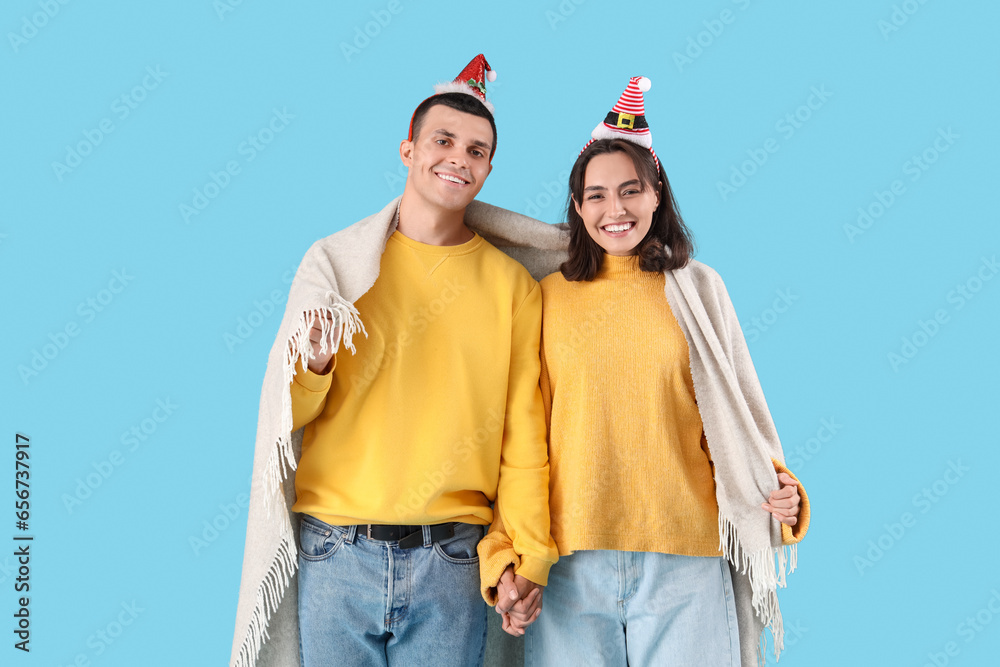 Happy young couple in Christmas hats with plaid on blue background