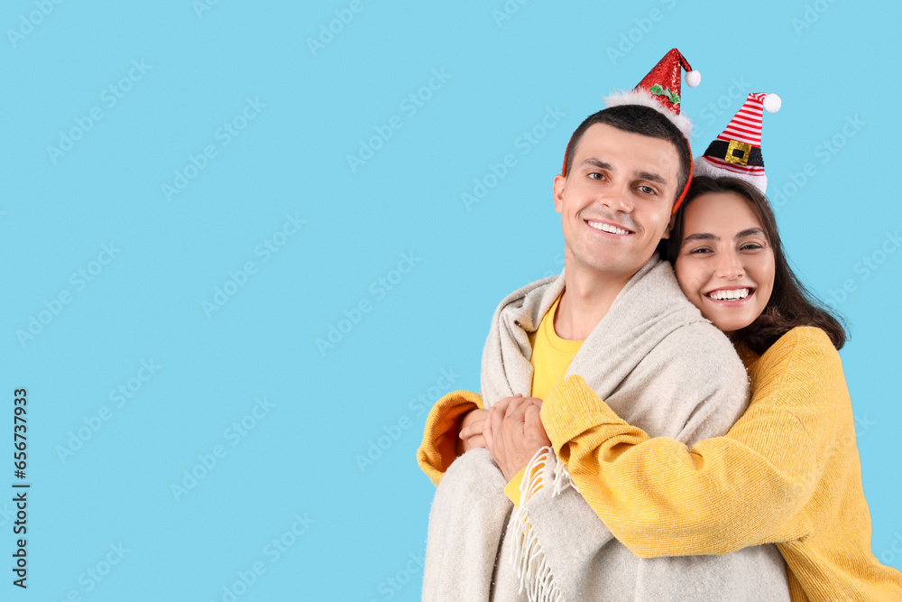 Happy young couple in Christmas hats with plaid on blue background