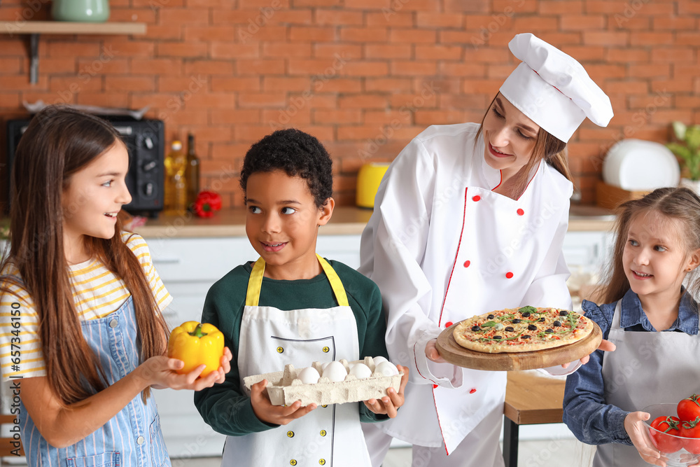 Female chef with prepared pizza and group of little children after cooking class in kitchen