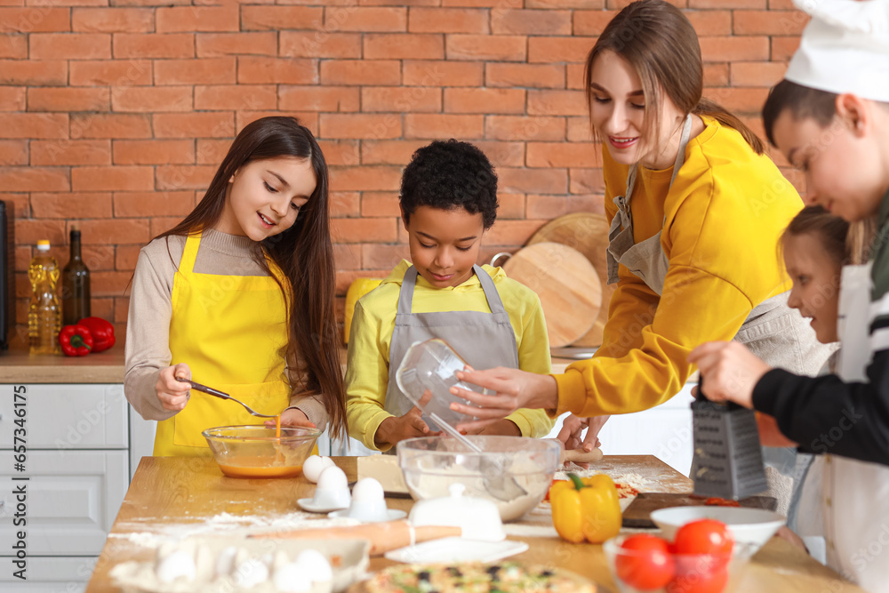 Female chef with group of little children preparing pizza during cooking class in kitchen