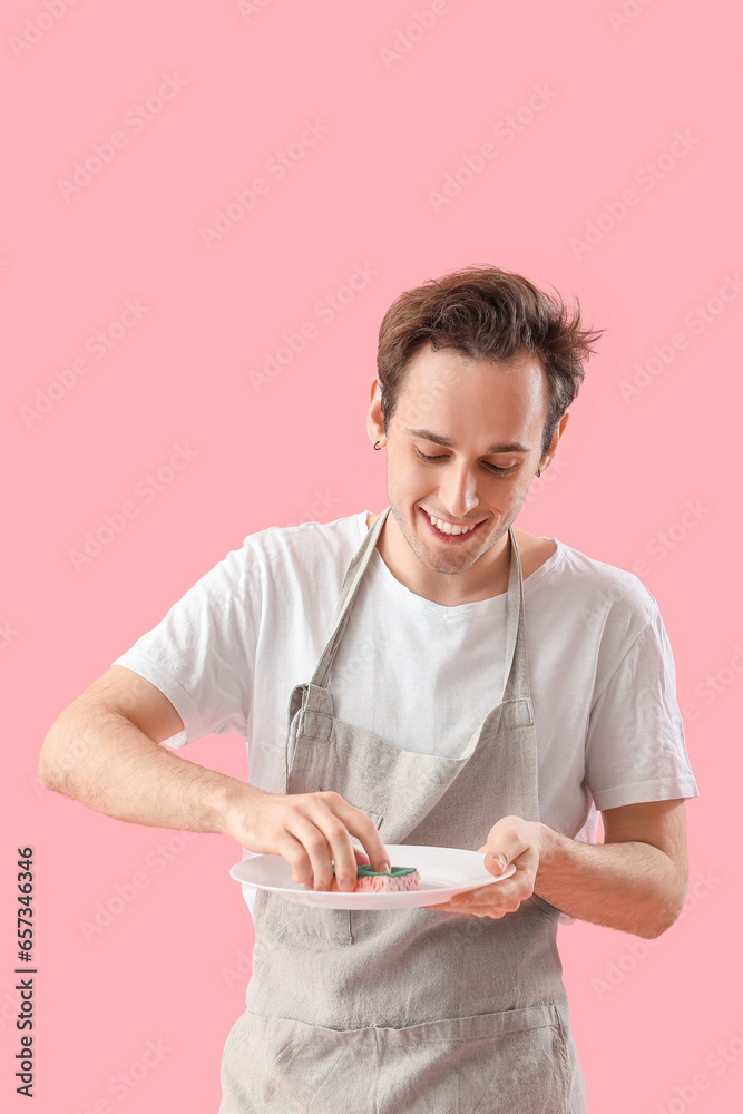 Young man washing dishes on pink background