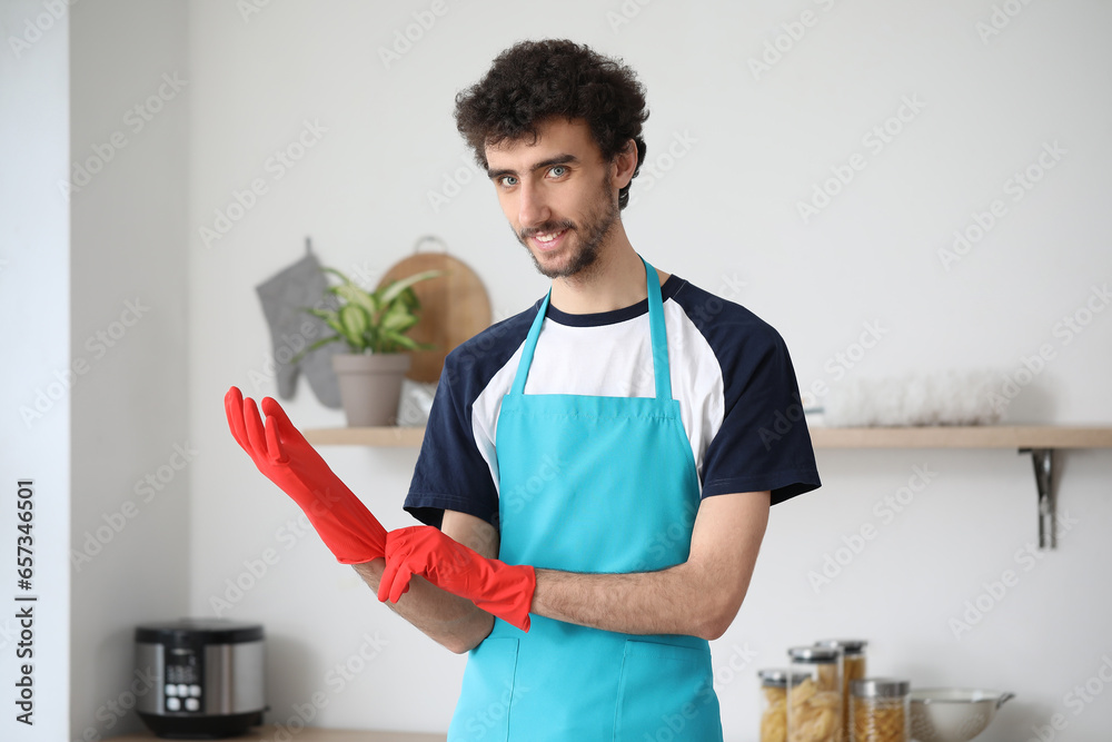 Young man putting rubber gloves in kitchen