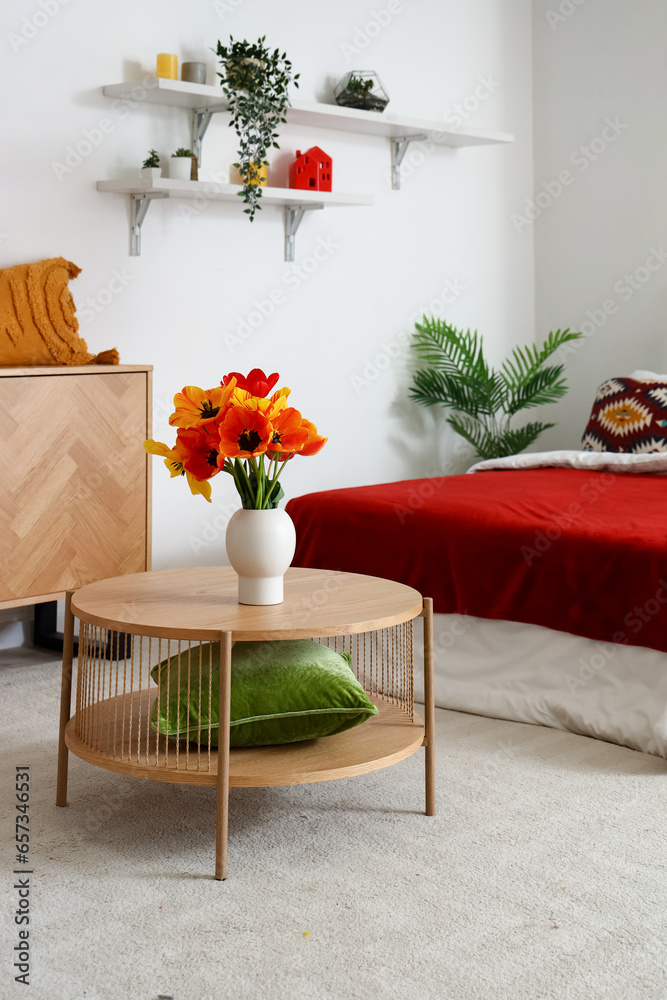 Interior of stylish bedroom with tulip flowers in vase on wooden table