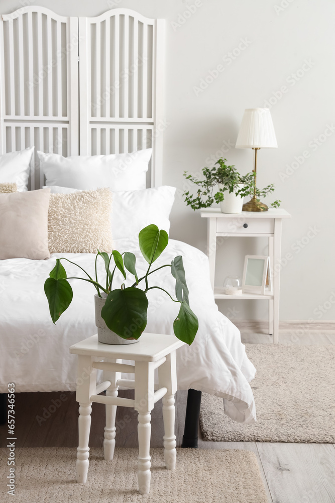 Interior of light bedroom with houseplant on bedside table