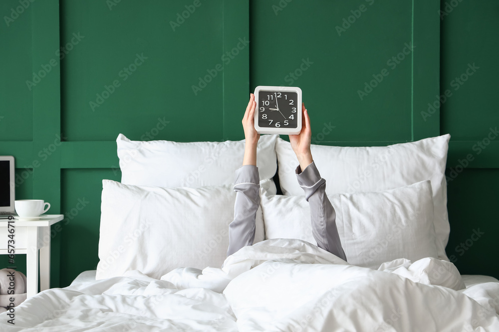 Morning of young woman with clock in bed