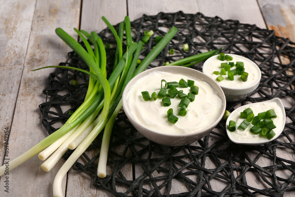 Bowls and gravy boat of tasty sour cream with sliced green onion on grey wooden background