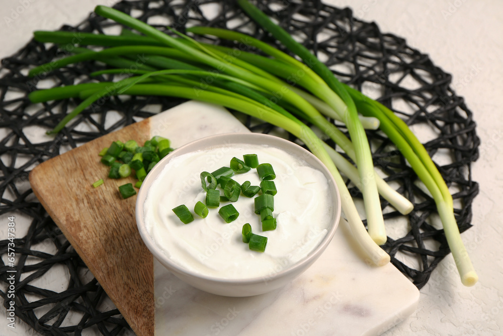 Board and bowl of tasty sour cream with sliced green onion on grey background