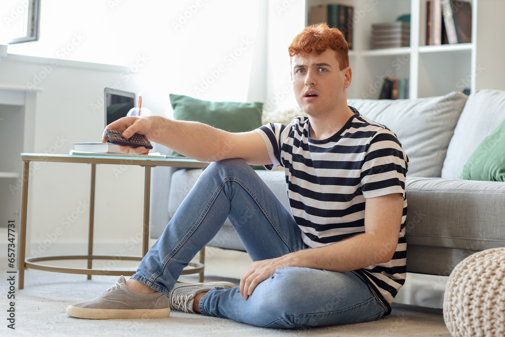 Shocked young redhead man watching TV at home