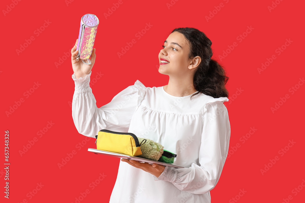 Female student with pencil cases and laptop on red background