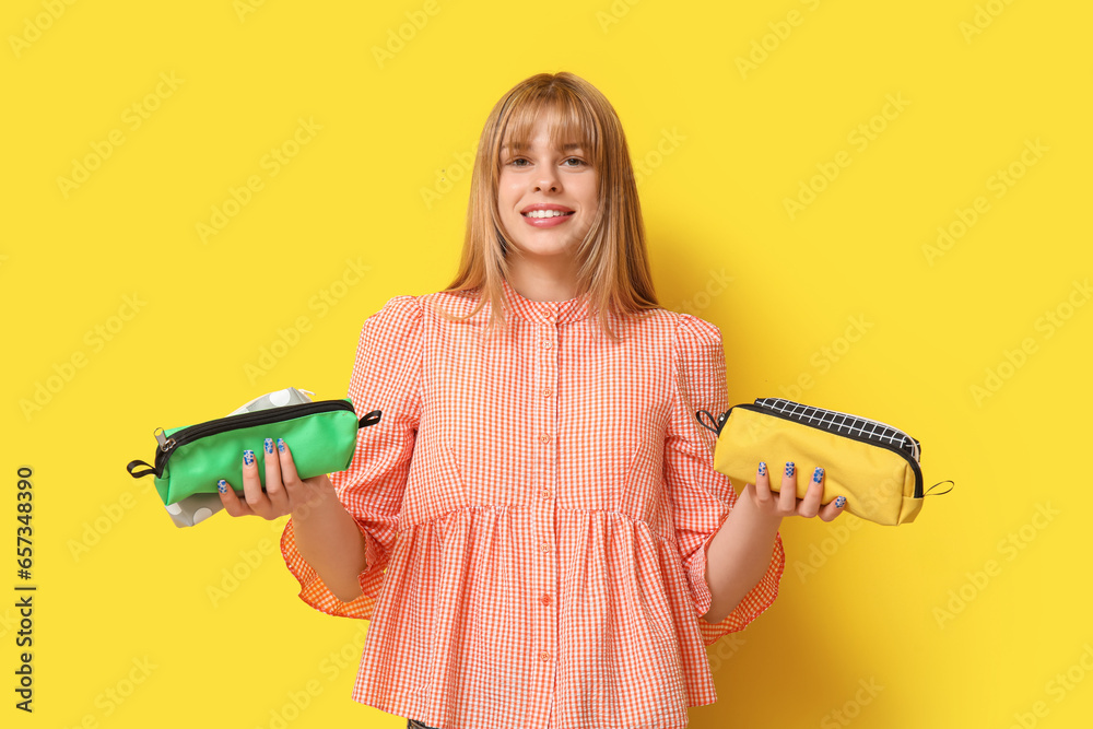 Female student with pencil cases on yellow background