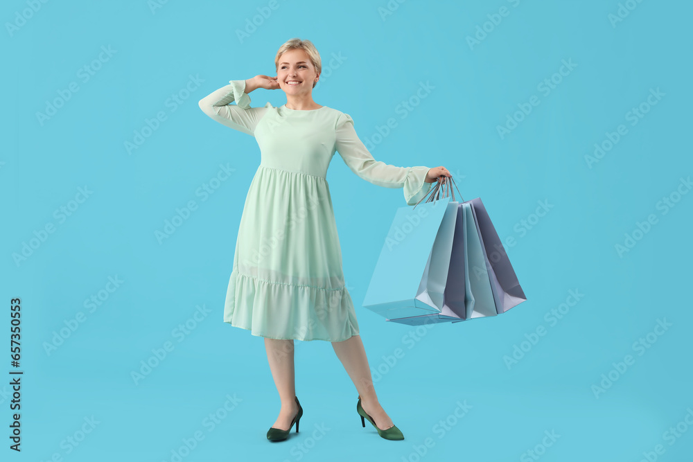 Happy beautiful young woman with shopping bags on blue background